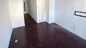 Um corredor com piso de madeira, paredes brancas e uma porta no final.
