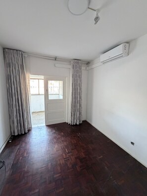 Une pièce dotée d’un plancher en bois, de murs blancs, d’un ventilateur de plafond et d’un appareil de climatisation.