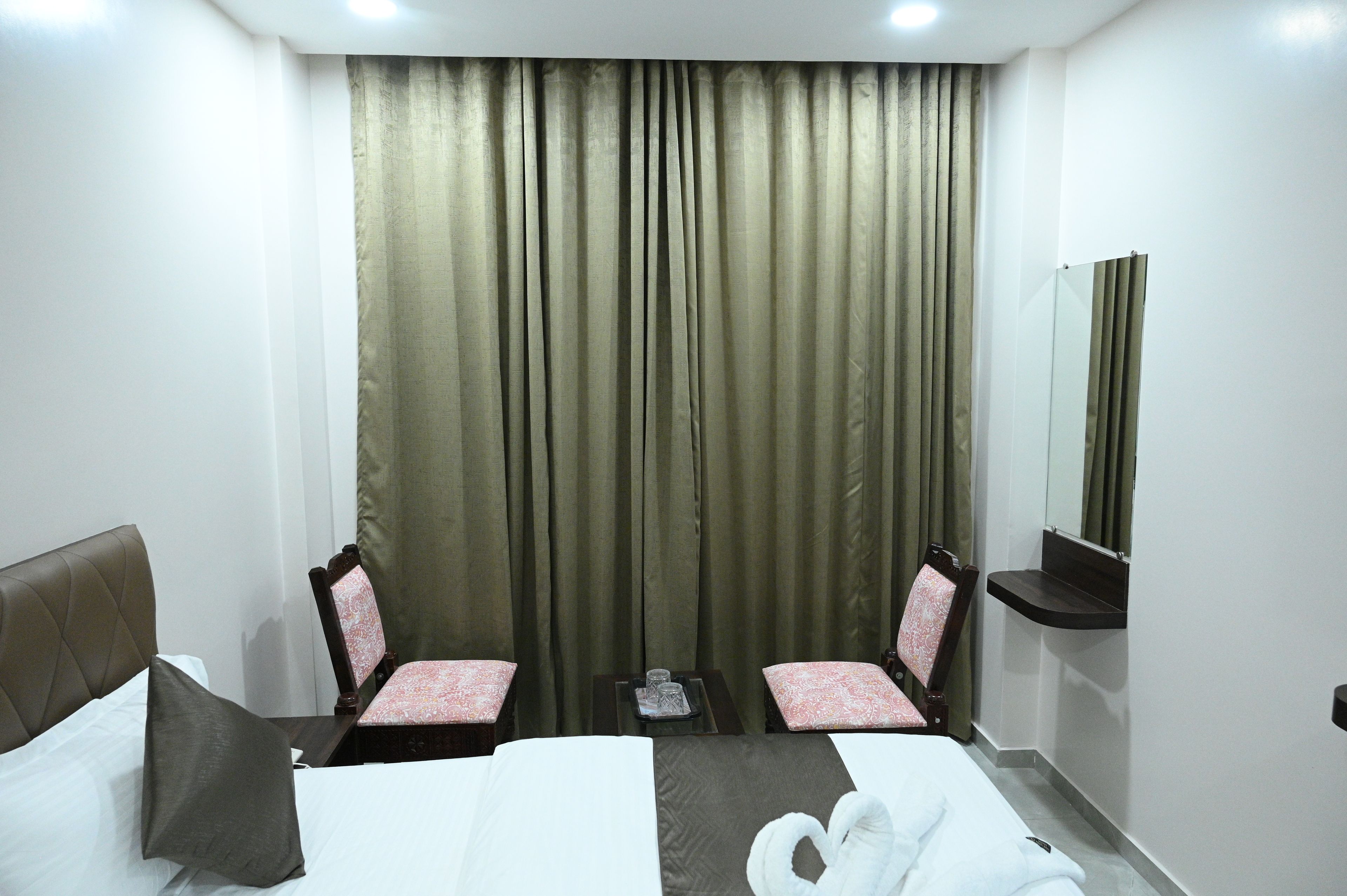 A hotel room with a bed, two chairs, a small table, a mirror, and a window with curtains.