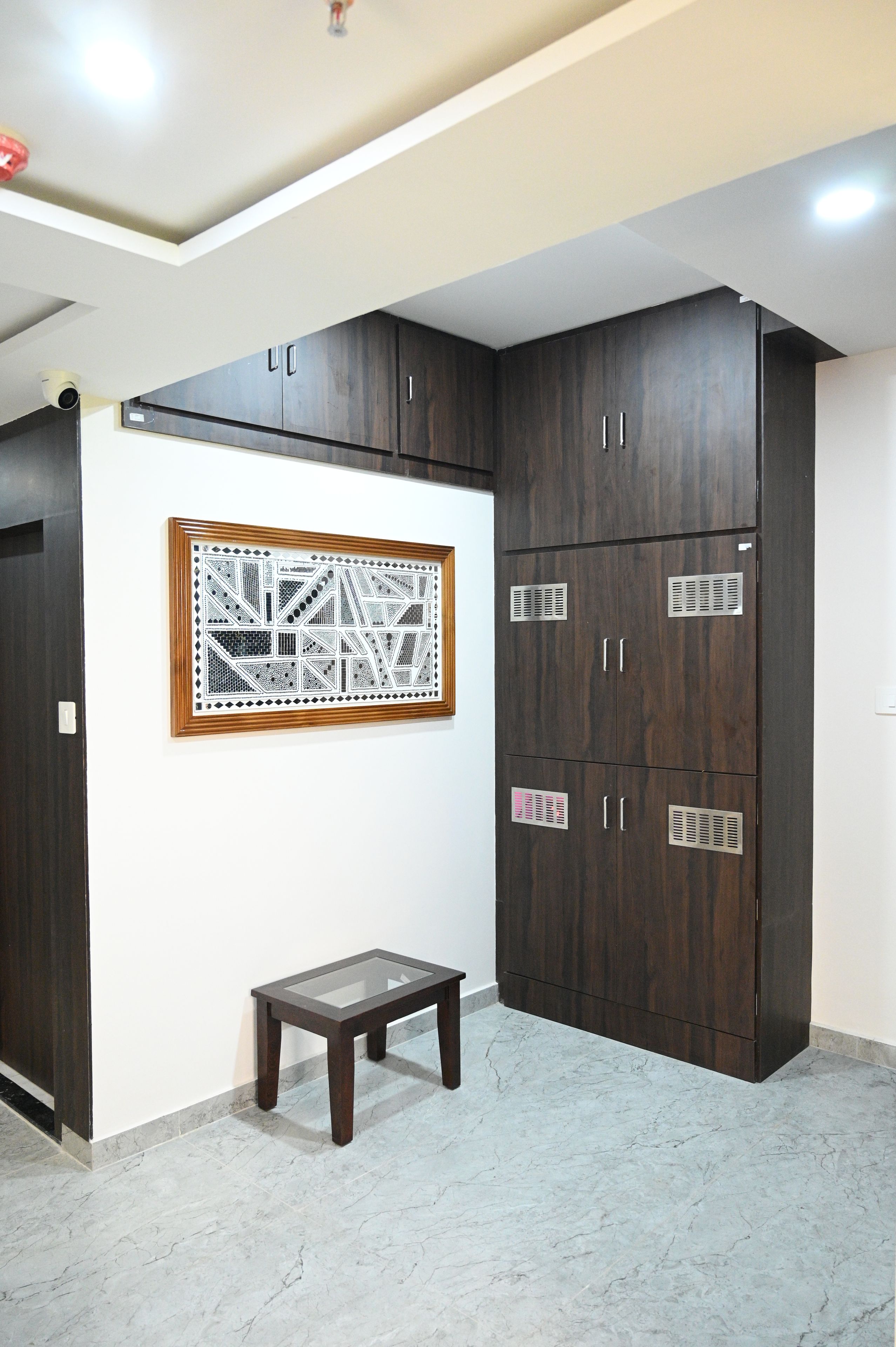 A room with a dark wooden wardrobe, a small wooden stool, and a framed geometric pattern on the wall.