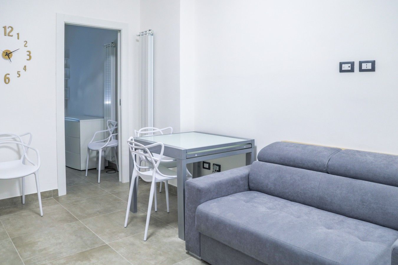 Un salon moderne avec un canapé gris, une table à manger avec des chaises et une horloge murale.