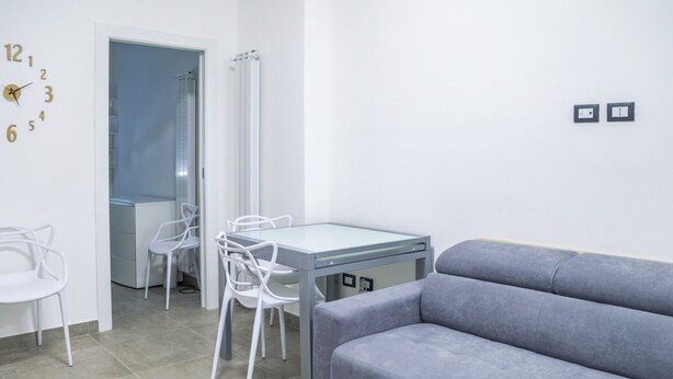 Una sala moderna con un sofá gris, una mesa de comedor con sillas y un reloj de pared.