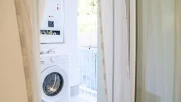 Uma lavanderia com máquina de lavar frontal, secadora, painel de controle e uma janela com vista para o exterior.