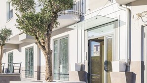 Entrada de un hotel con puerta de vidrio, un árbol en primer plano y un letrero de no estacionamiento.