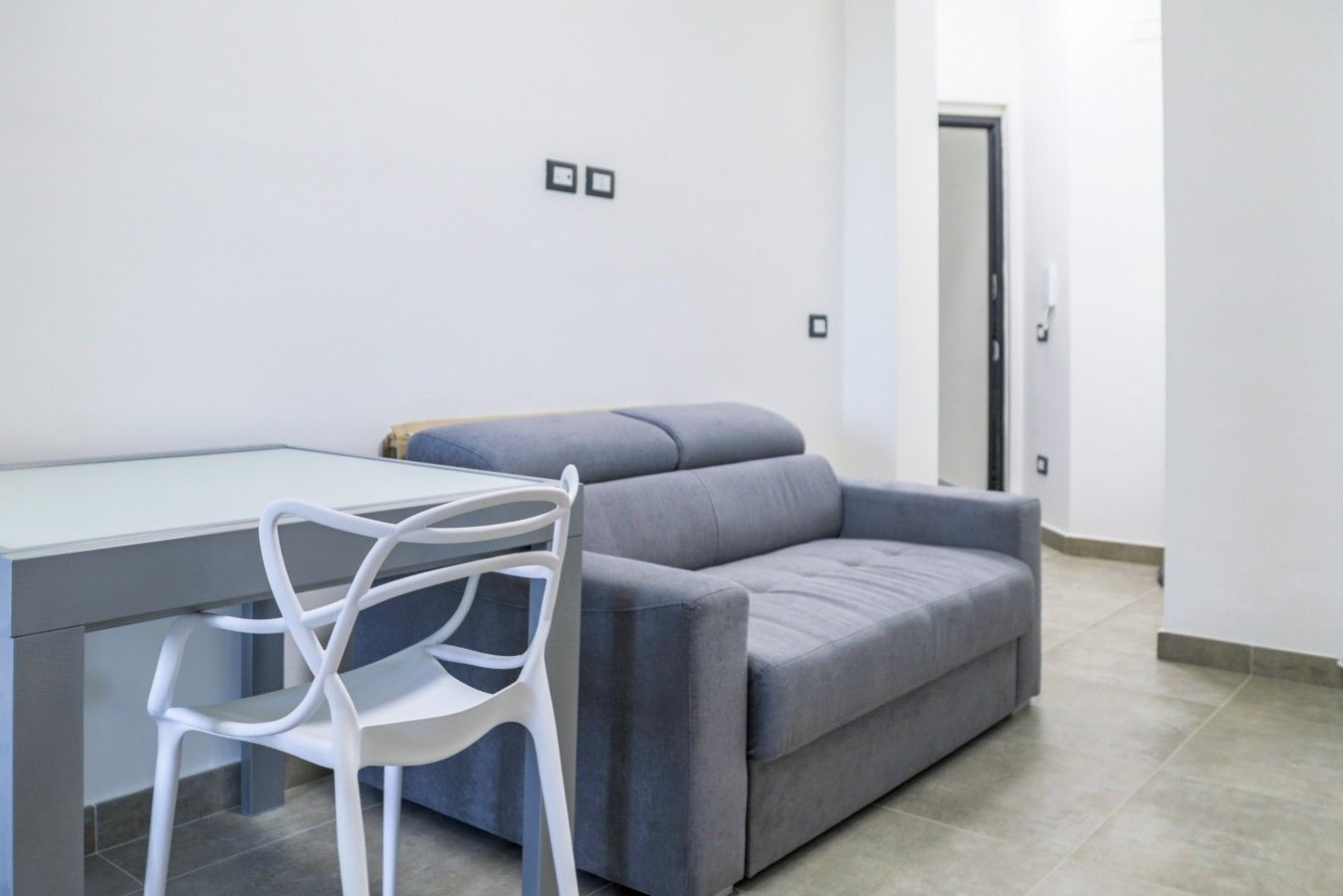 Un salon moderne avec un canapé gris, un fauteuil blanc et une table dont le plateau est en verre.