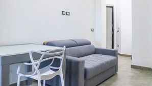 Una sala de estar moderna con un sofá gris, una silla blanca y una mesa con cubierta de vidrio.