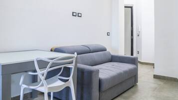 Un salon moderne avec un canapé gris, un fauteuil blanc et une table dont le plateau est en verre.