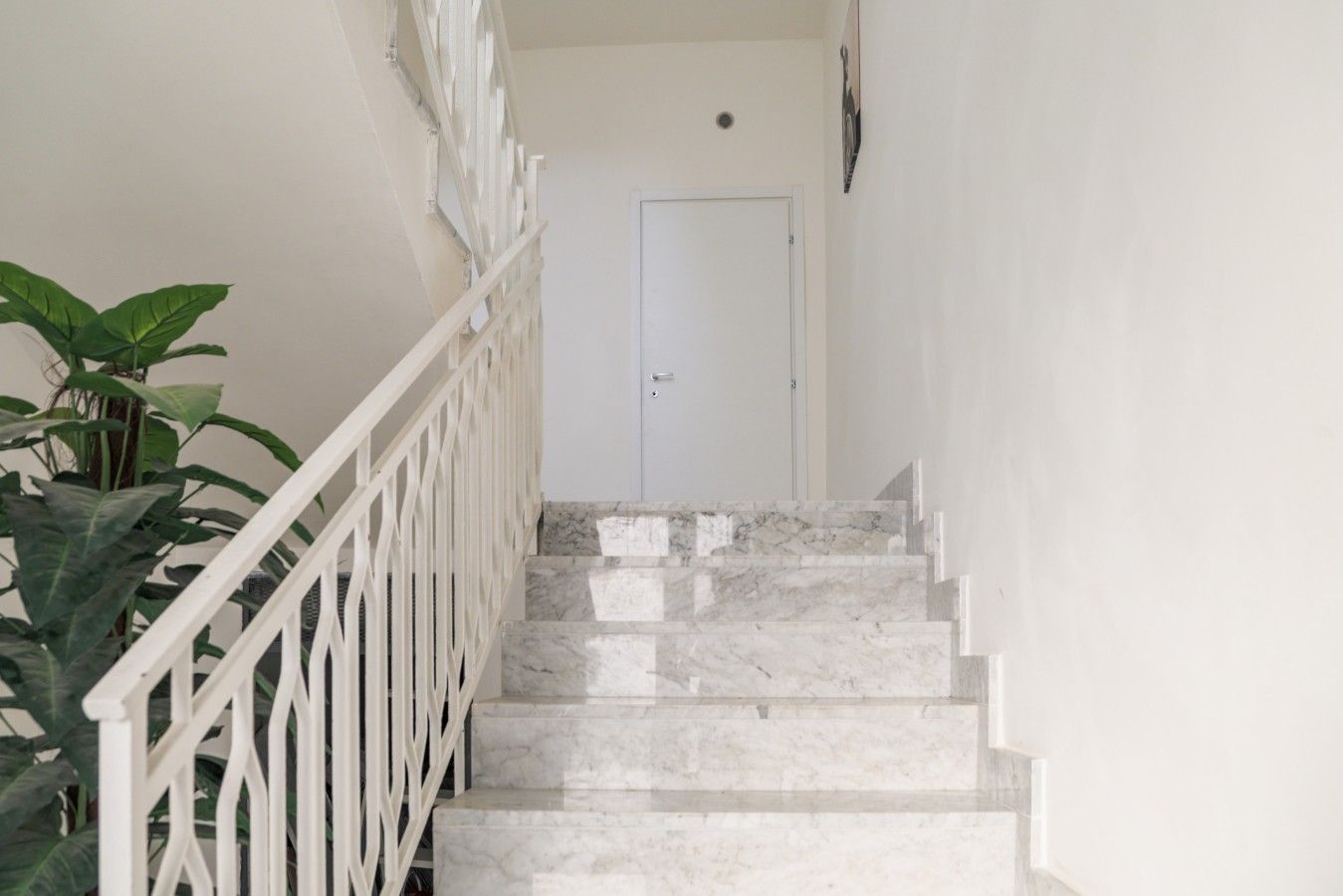 Un escalier avec des rampes blanches et des marches en marbre menant à une porte blanche.