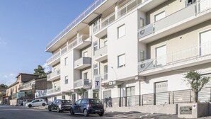 Un edificio residencial de varios pisos con balcones, un estacionamiento con coches y un cielo despejado.