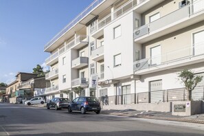 Un edificio residencial de varios pisos con balcones, un estacionamiento con coches y un cielo despejado.