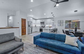 A modern kitchen with white cabinets, stainless steel appliances, and a dining area with a blue sofa and a small table. - Margaret Manor - South Lake Tahoe Retreat (South Lake Tahoe)