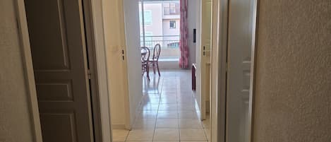 A hallway with a tiled floor leading to a balcony with chairs and a table.