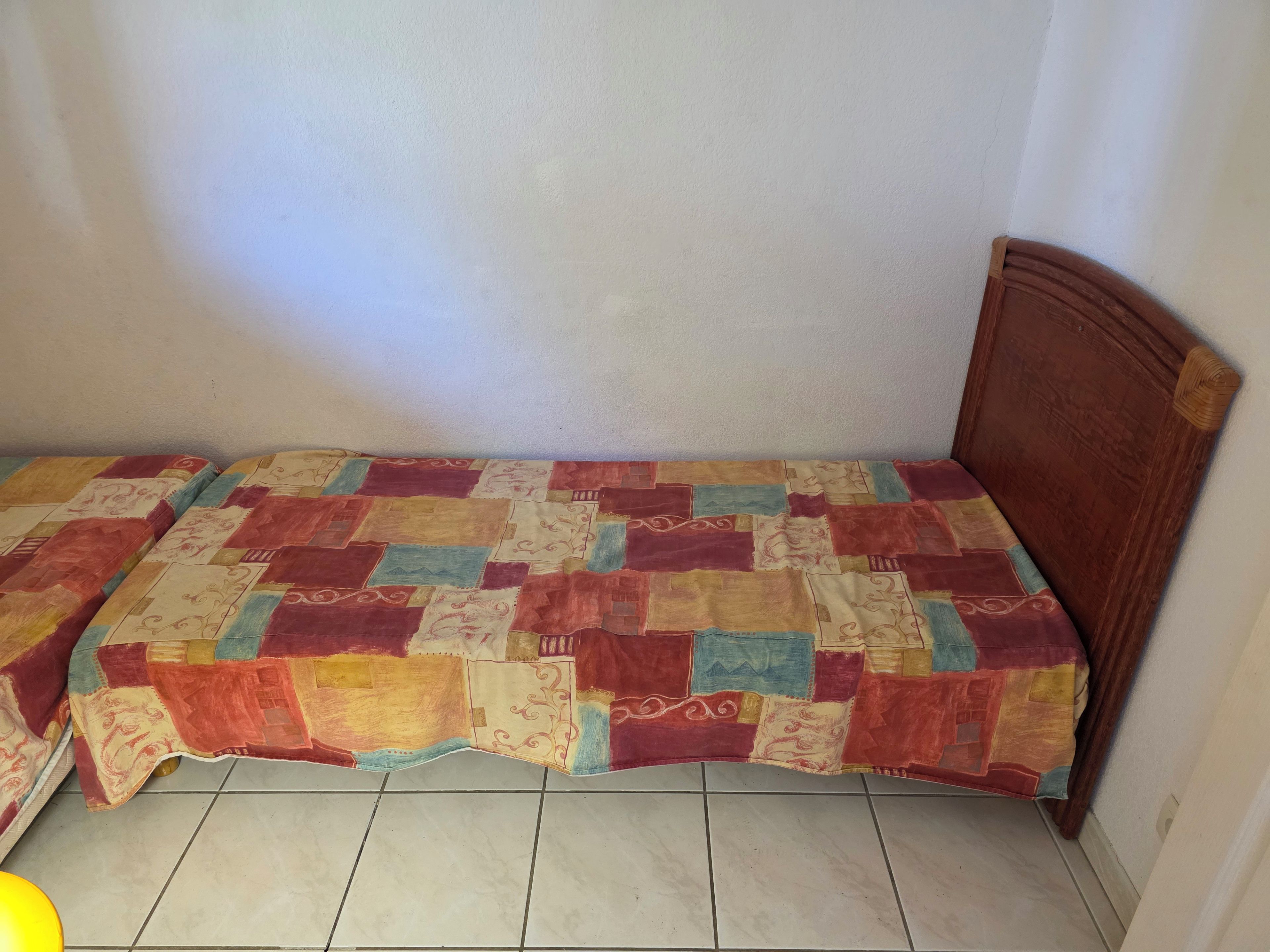 A small, single-bed room with a wooden headboard, a patchwork quilt, and tiled flooring.