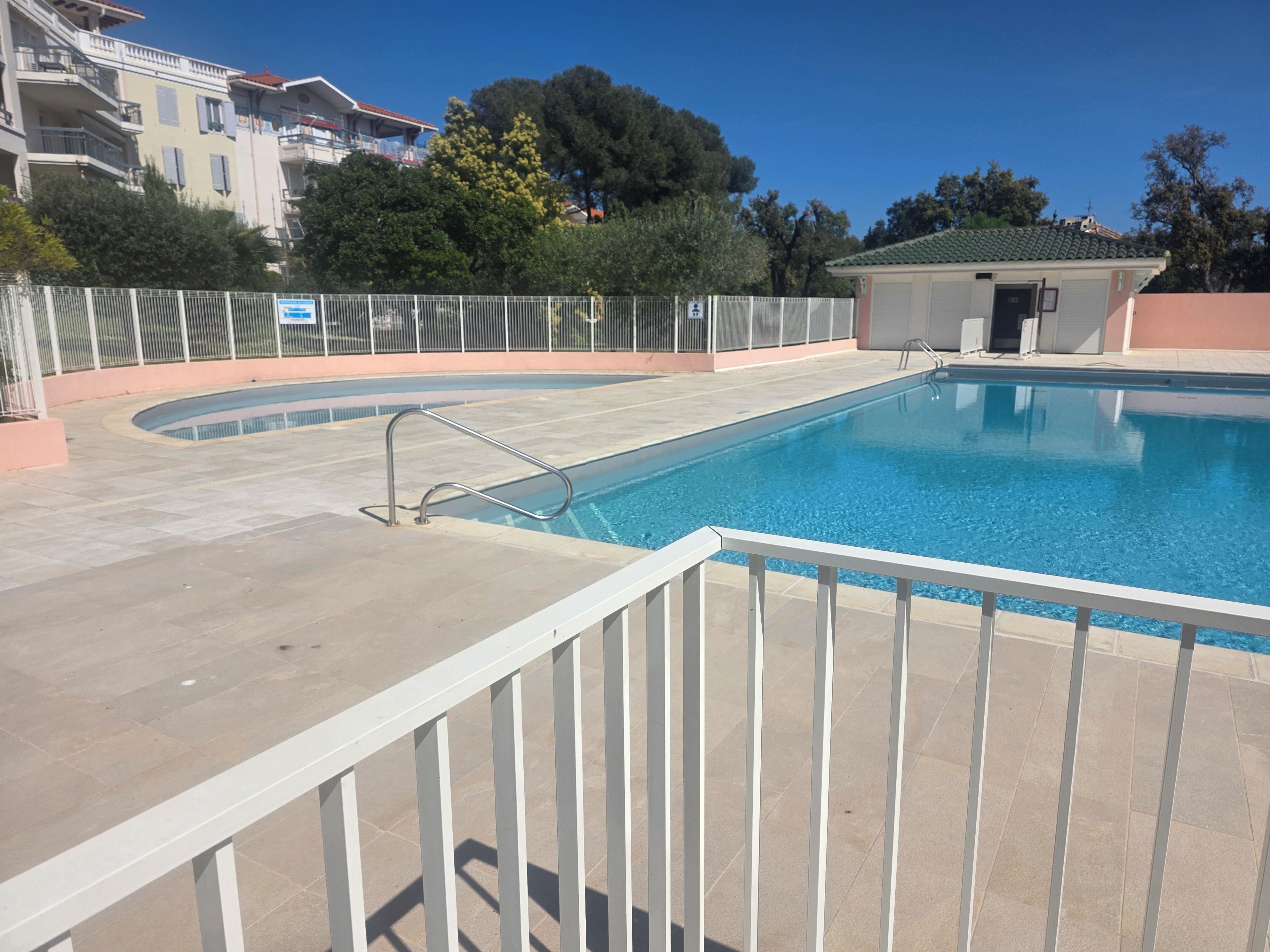 Une piscine entourée d’une clôture blanche, un petit bâtiment et un ciel dégagé.