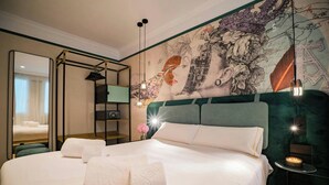 Quarto de hotel com uma cama grande, um espelho, uma parede com um mural detalhado e uma pequena mesa com uma vela.