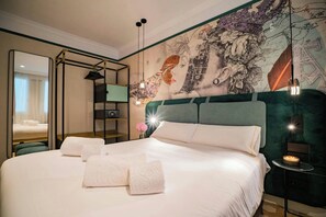 Una camera d'albergo con un letto grande, uno specchio, una parete decorata con un affresco e un tavolino con una candela.