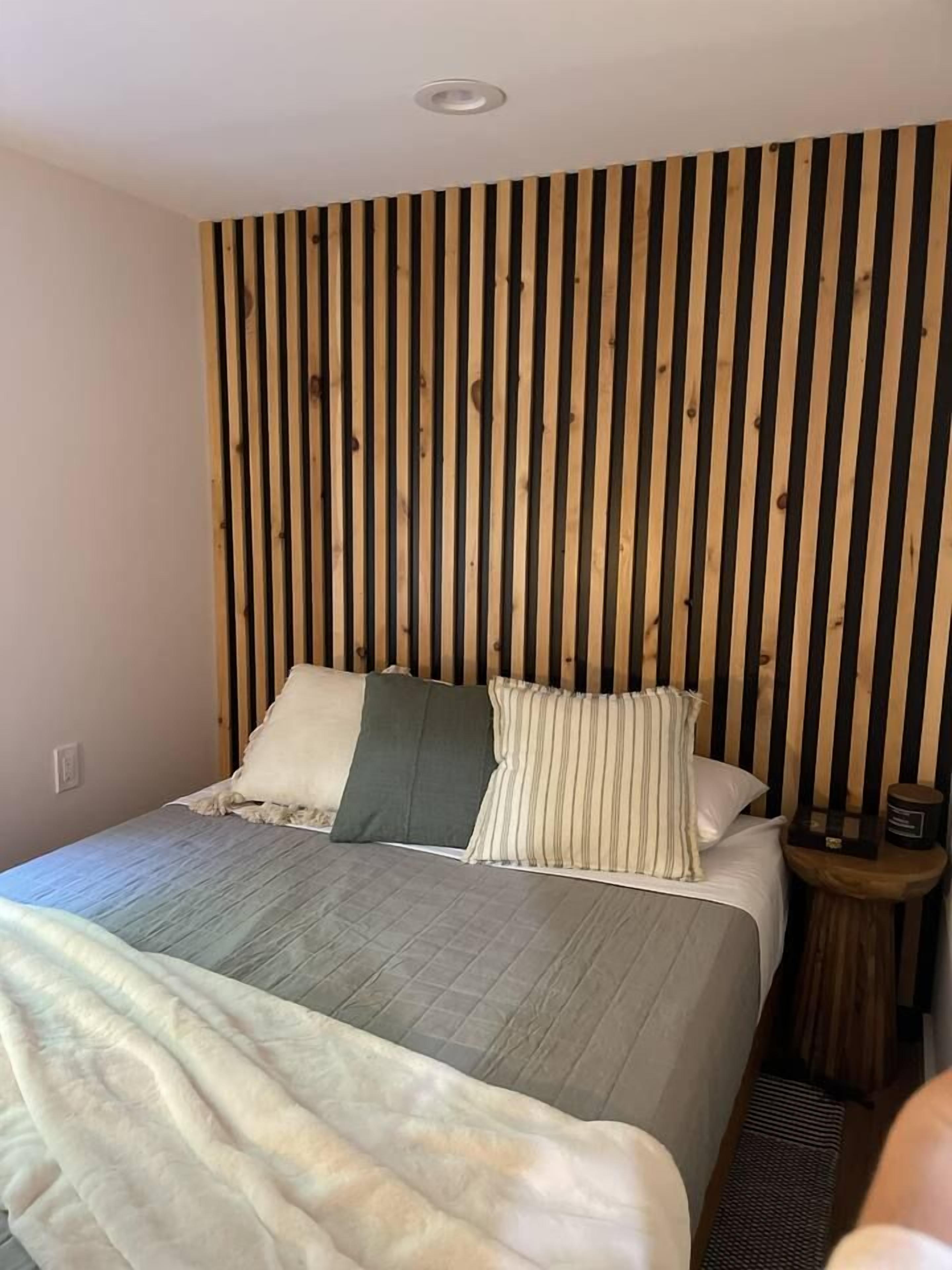 A bedroom with a bed, pillows, a bedside table, and a wooden slat wall.