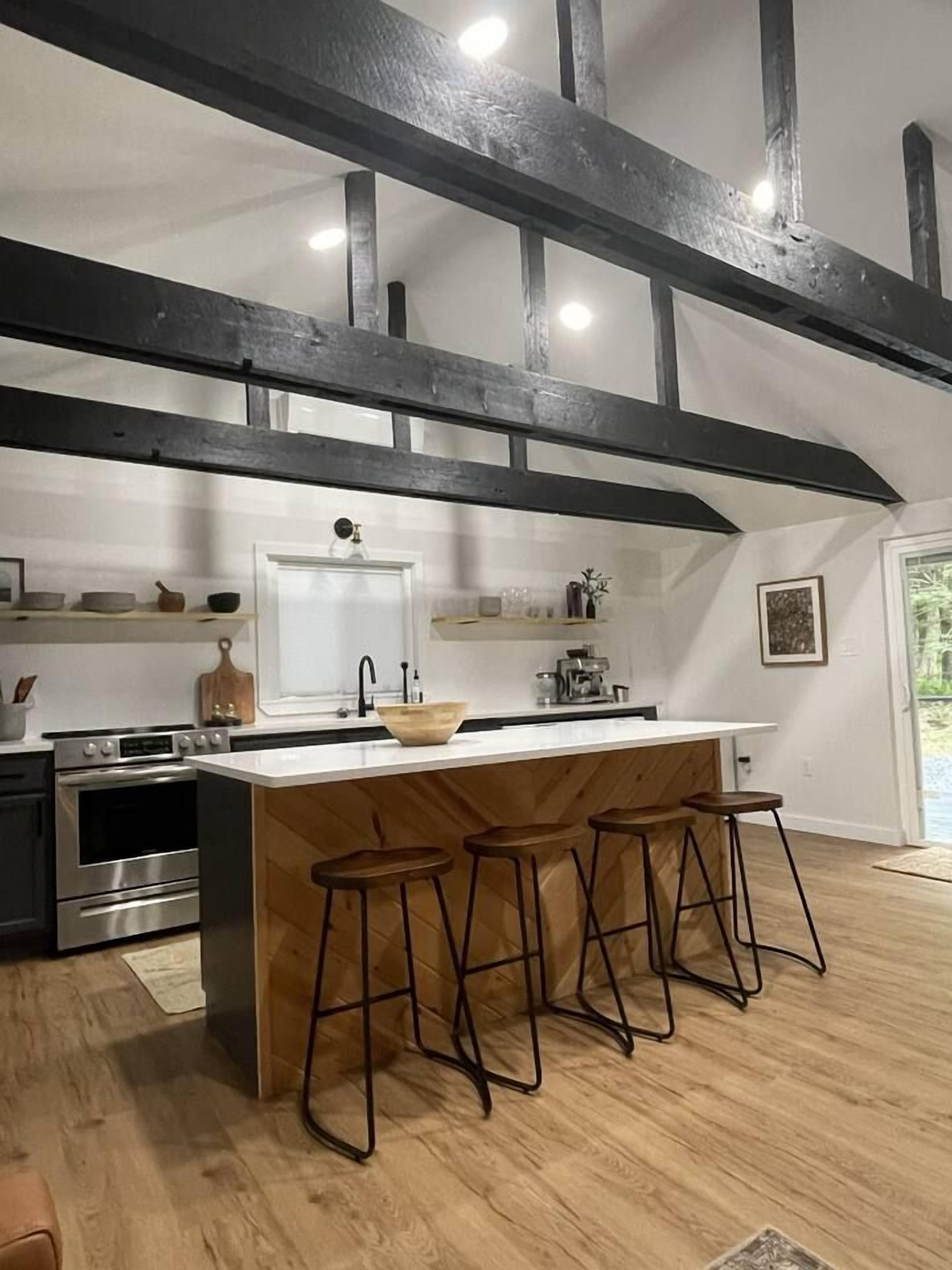 A kitchen with a central island, bar stools, a stove, and a large window.
