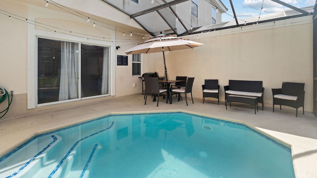 An indoor swimming pool with a table and chairs, a covered seating area, and a sliding glass door.