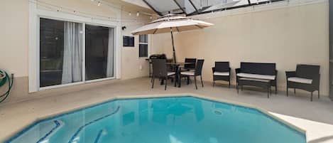 An indoor swimming pool with a table and chairs, a covered seating area, and a sliding glass door.