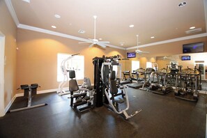 Ein Fitnessraum mit verschiedenen Trainingsgeräten, einem Deckenventilator und einem Fernseher an der Wand.
