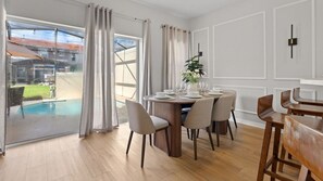 A dining area with a round table, chairs, and a view of a swimming pool through large glass doors. - 4BR Bella Vida Resort Pool & BBQ Near Disney (Kissimmee)