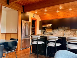 Eine moderne Küche mit Edelstahl-Kühlschrank, dunklen Schränken, einer Steinrückwand und einer Theke mit Hockern.