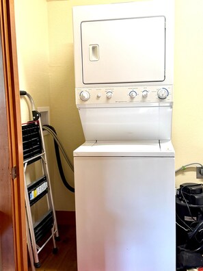 A front-loading washing machine with a control panel, a power cord, and a metal shelf unit with a power strip. - NEW LISTING! Cozy Big Sky Luxury Escape- Ski In/Ski Out -Private outdoor hot tub (Big Sky)