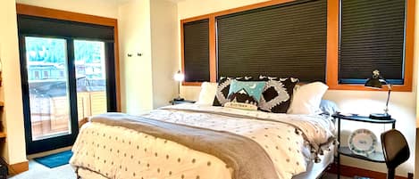 Un dormitorio con una cama, una mesita de noche, una lámpara y vistas al exterior a través de una puerta.