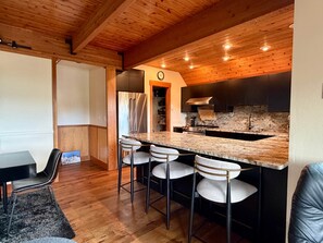 A modern kitchen with a wooden ceiling, a stainless steel refrigerator, a marble countertop, and bar stools. - NEW LISTING! Cozy Big Sky Luxury Escape- Ski In/Ski Out -Private outdoor hot tub (Big Sky)