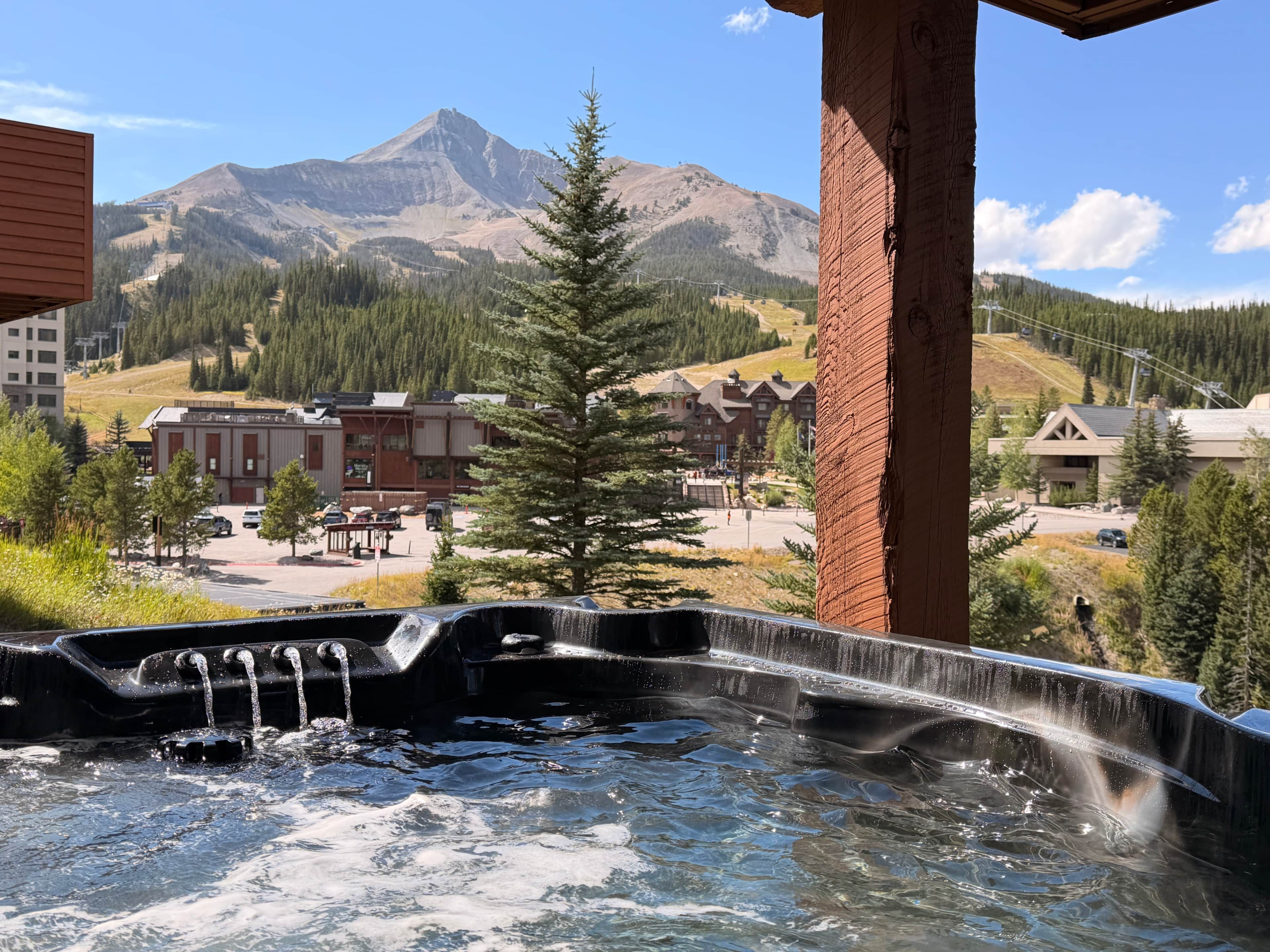 A hot tub with a mountain view, a wooden structure, and a building in the background.