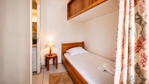 A small, single-bed room with a wooden headboard, a bedside lamp, a small round table, and a washing machine in the corner. - Studio with terrace, swimming pool and parking (Guérande)