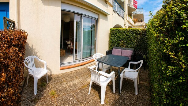 A patio area with a table and chairs, a sliding glass door, and a hedge. - Studio with terrace, swimming pool and parking (Guérande)