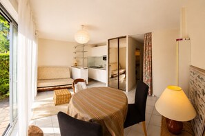 Ein Zimmer mit Esstisch, Stühlen, einer Couch, einer Lampe und Blick ins Freie.