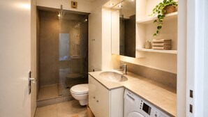 A modern bathroom with a glass-enclosed shower, a toilet, a sink, a mirror, and a washing machine. - Studio with terrace, swimming pool and parking (Guérande)
