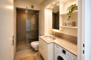 A modern bathroom with a glass-enclosed shower, a toilet, a sink, a mirror, and a washing machine. - Studio with terrace, swimming pool and parking (Guérande)