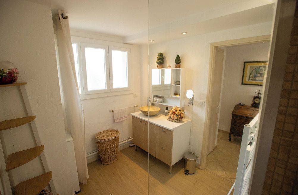 Un baño con piso de madera, un lavamanos blanco, un espejo y un mueble pequeño.