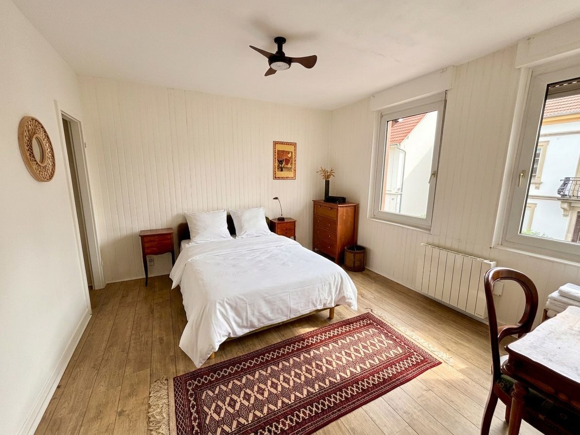 A bedroom with a bed, a wooden nightstand, a dresser, a radiator, and a window with a view.