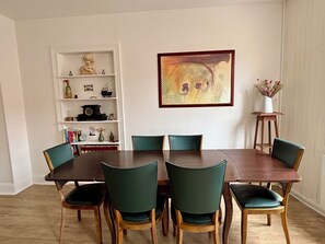 Ein Essbereich mit einem Holztisch, sechs Stühlen, einem Bücherregal mit verschiedenen Gegenständen und einem Gemälde an der Wand.