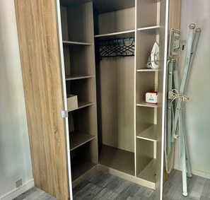 Ein begehbarer Kleiderschrank mit mehreren Regalen und Platz zum Aufhängen, ein Staubsauger und eine Mehrfachsteckdose auf dem Boden.