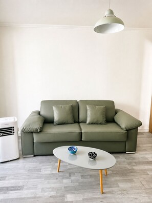 Ein Wohnzimmer mit einem grünen Sofa, einem weißen Couchtisch und einer Deckenleuchte.
