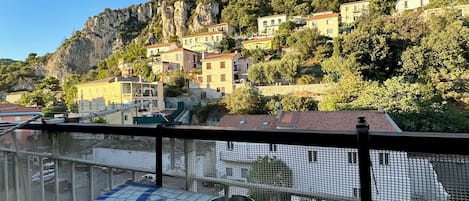 A balcony with a tiled floor, overlooking a hillside with buildings and greenery.
