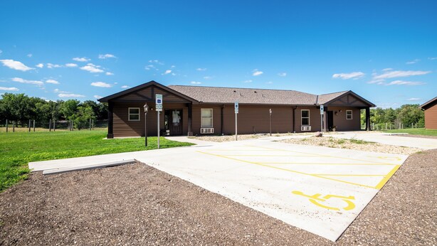 A building with a parking lot marked with handicapped parking spaces. - Located in Peoria, Illinois Legacy Cabin 8 offers a luxury retreat immersed in nature, with stunning views of roaming bison and elk just outside your window. This 2-bedroom, 1-bath cabin features a comfortable living area with plush seating and a coz (Hanna City)