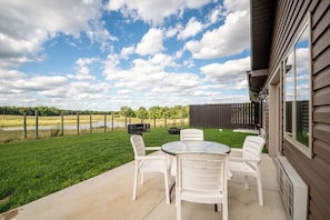 Un patio exterior con mesa y sillas, una parrilla y vistas a un campo de césped y árboles.