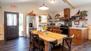 A modern kitchen with wooden cabinetry, a central island, and a dining area with wooden chairs. - Located in Peoria, Illinois Legacy Cabin 8 offers a luxury retreat immersed in nature, with stunning views of roaming bison and elk just outside your window. This 2-bedroom, 1-bath cabin features a comfortable living area with plush seating and a coz (Hanna City)