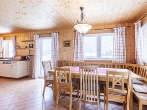 A wooden cabin interior with a dining table, chairs, a kitchen area, and large windows with curtains. - Cabin in Annaberg With Swimming Pool (Annaberg-Lungoetz)