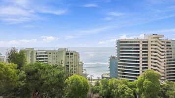 A coastal cityscape with modern high-rise buildings, a clear sky, and a view of the ocean.