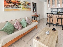 A living room with a sofa, a coffee table, and a dining area with chairs and a kitchen in the background.
