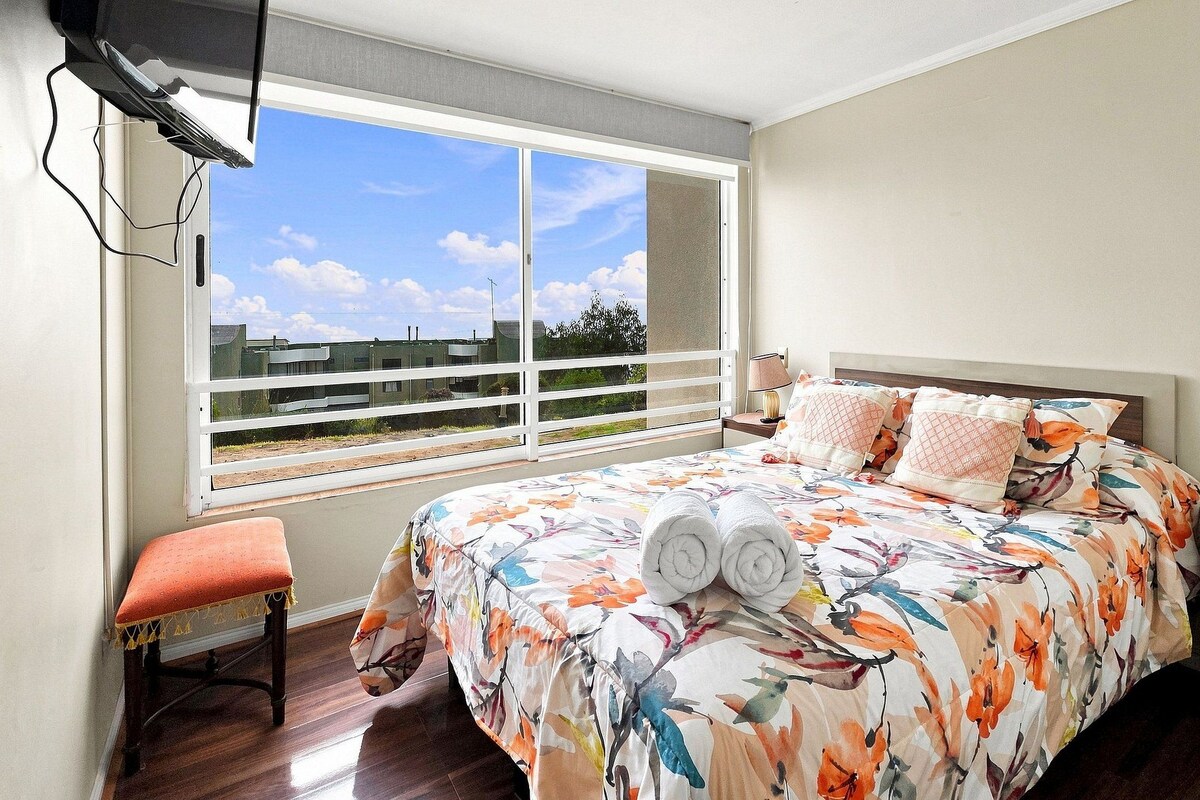Un dormitorio con una cama grande, una ventana con vistas, una mesita de noche y una silla.