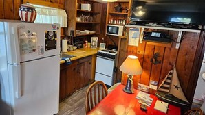 Una cocina con paredes de madera, un refrigerador, un microondas, una estufa, una mesa con una lámpara y un televisor.
